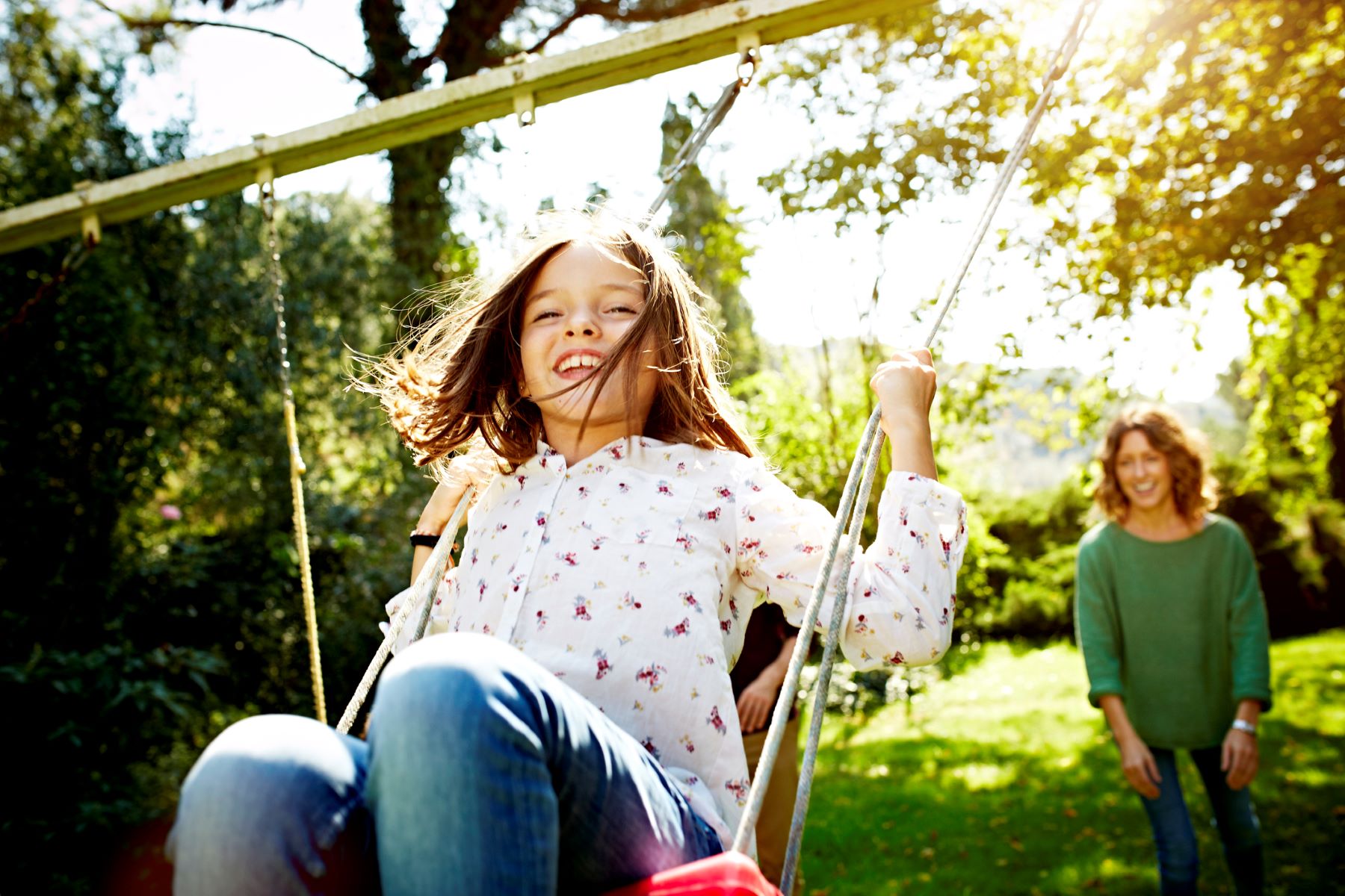 girl being pushed on a swing by her mom in the background